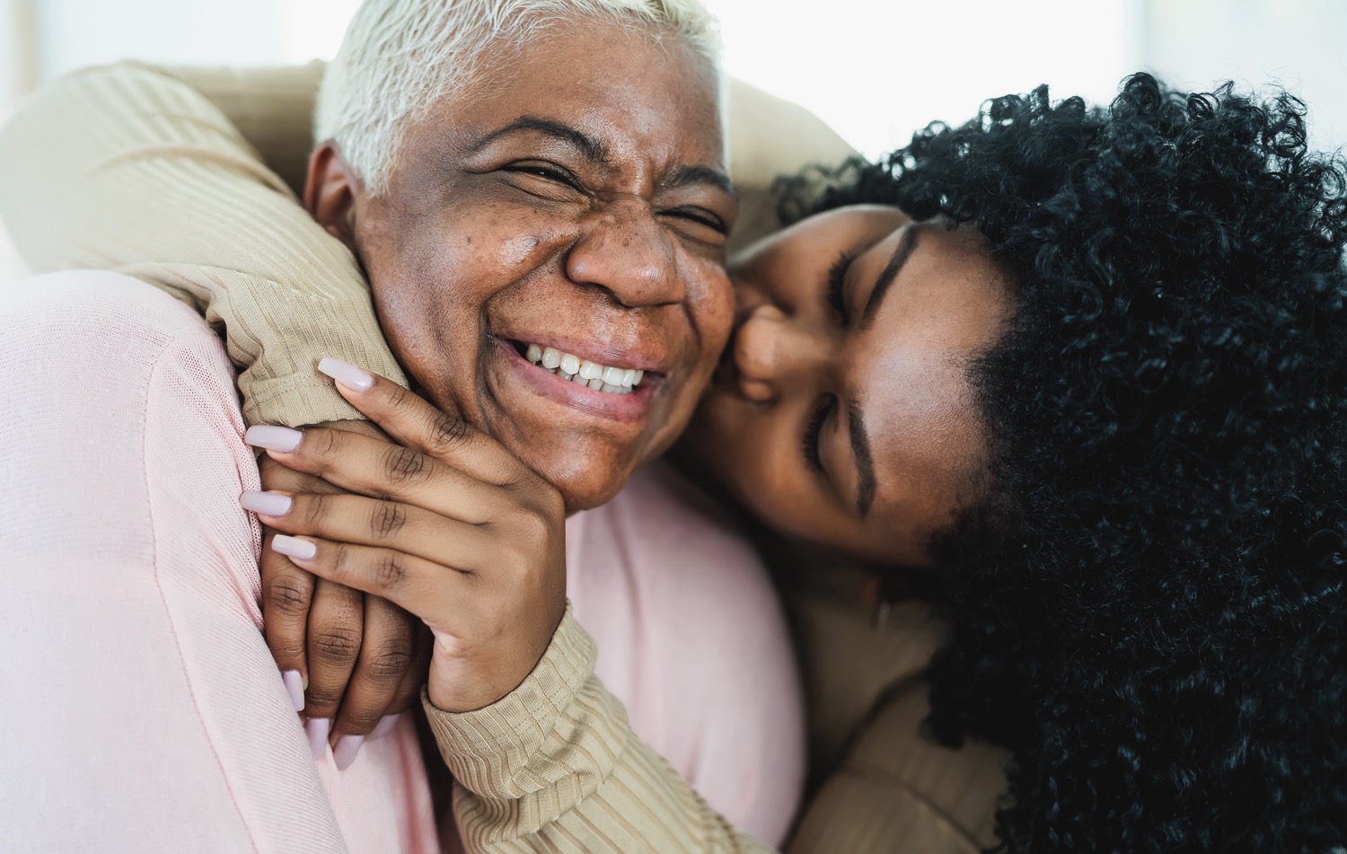 A happy black grandmother gets a hug and kiss on the cheek from her adult granddaughter.